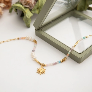 Detail of beaded necklace with freshwater pearls and gold sun charm on white background