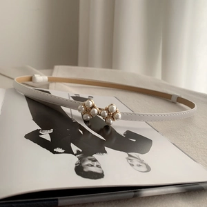 Detailed view of white slim leather belt with a pearl-studded golden bow buckle