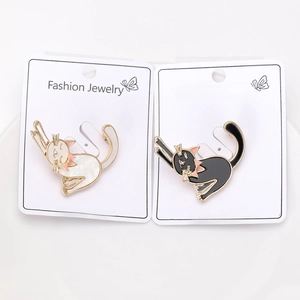 Detail view of black and white enamel cat brooches with gold metal frame on a display card