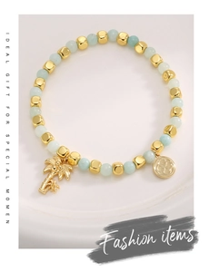 Close-up of gold-plated palm tree charm and light green beads on a bohemian bracelet