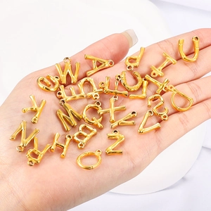 Golden bamboo texture alphabet charms for DIY jewelry making held in hand for scale