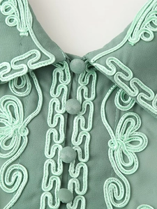 Détail de la broderie florale vert menthe et boutons en tissu sur l'encolure d'une robe