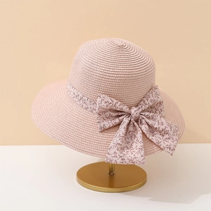Détail d'un chapeau de soleil rose en paille avec un nœud floral sur support doré