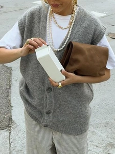 Dettaglio di un gilet in maglia grigio con bottoni e una borsa marrone in stile streetwear