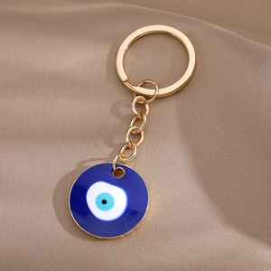 Detailed close-up of golden keychain with blue enamel Turkish Evil Eye charm on brown fabric