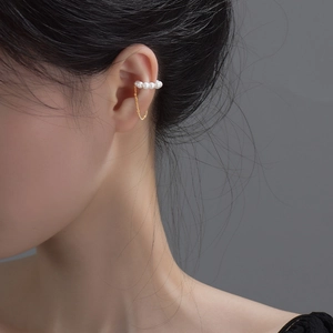 Detailed close-up of a gold-plated pearl ear cuff with a delicate hanging tassel chain
