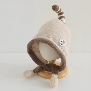 Detail view of winter knitted baby hat with penguin patch and soft pom-pom ties