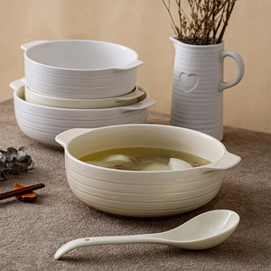 Large cream ceramic soup bowl with handles and matching spoon on textured tabletop
