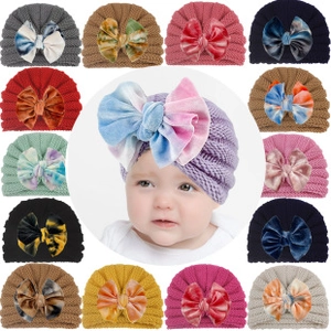 Detailed view of various colorful knitted baby hats with large velvet bows in multiple colors