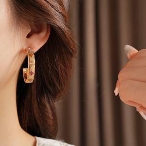 Close-up of model wearing gold wide C-shape hoop earrings with colorful gemstones