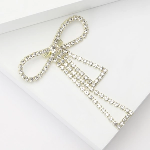 Detailed view of a gold bow brooch with sparkling rhinestones and long tassel chains