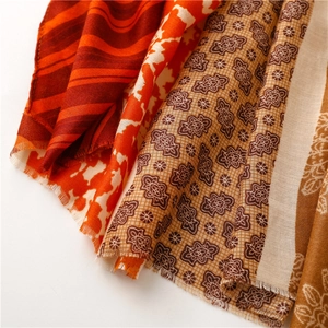 Detail of red wavy patterns and orange dotted floral print on scarf with fringe edge