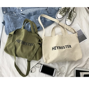 Detail of large canvas tote bags in olive green and beige with HEYMISTER printed logo