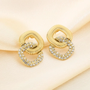Detail of gold-plated intertwined earrings with ribbed texture and white zircon stones