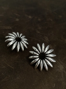 Detail view of silver hollow floral earrings with polished petals on dark leather