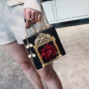 Macro view of vintage black square bag with gold floral embossed frame and red rose detail