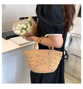 Detail view of woven straw tote bag with colorful embroidery held by a model