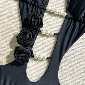 Detail of black one-piece swimsuit with 3D fabric roses and white pearl string cutouts