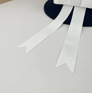 Detailed view of long white grosgrain ribbon streamers on a navy JK uniform wool hat