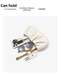 Spacious interior of cream pleated cloud bag holding phone, perfume and sunglasses