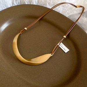 Macro shot of matte gold crescent moon pendant with brushed texture on minimalist necklace