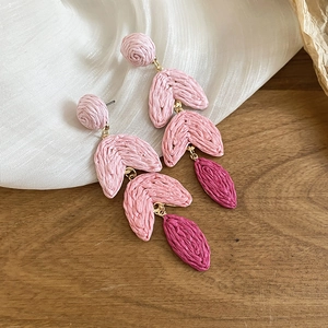Macro detail of pink and burgundy raffia tassel earrings with gold-tone hardware on wood