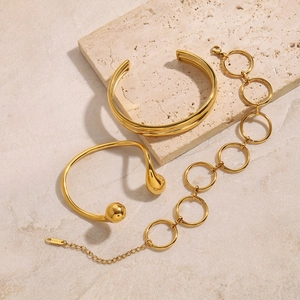 Three-piece set of elegant gold stainless steel bracelets on a textured stone background