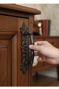Close-up of a vintage black cast iron door handle mounted on a brown wooden cabinet