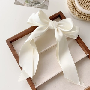 Detailed view of a large white satin bow hair clip with streamers on a wooden tray