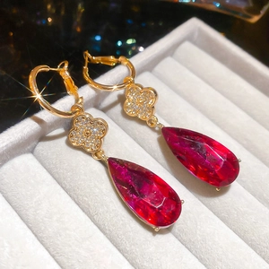 Macro view of gold clover earrings with sparkling diamonds and red water drop pendants