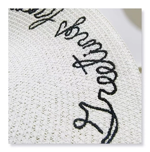 Macro shot of black cursive embroidery on a white woven straw hat for summer protection