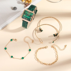 Flat lay of women's square emerald watch set with gold butterfly bracelets on beige table