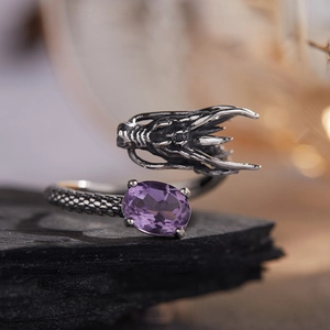 Macro shot of a dragon-shaped silver ring with an oval purple gemstone on black rock