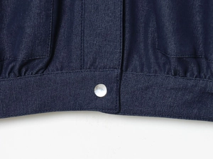 Close-up of navy denim bomber jacket hem featuring silver metal button and fine stitching