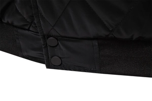 Detail of black quilted jacket featuring diamond stitching and ribbed hem with dual snaps