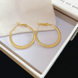Détail de boucles d'oreilles rondes dorées mates sur une boîte cadeau blanche à texture sablée