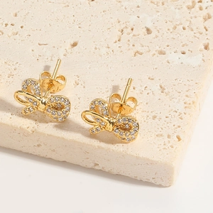 Macro detail of golden bow earrings with micro-pave white zircon on beige stone texture