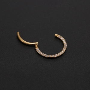 Macro shot of hinged gold piercing ring with channel-set cubic zirconia on black surface