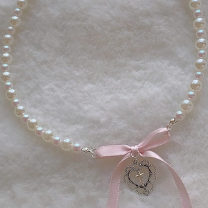 Detail of pink satin bow and silver hollow heart pendant on white pearl necklace