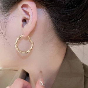 Detailed view of gold twisted rope hoop earrings worn on a female model