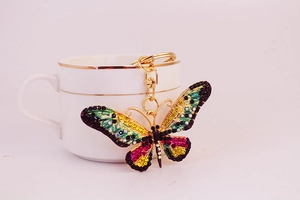 Close-up of golden butterfly keychain with colorful rhinestones beside a white ceramic cup