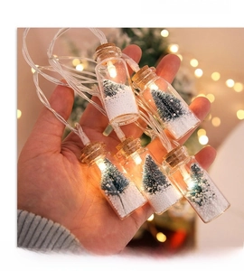Hand holding a decorative LED glass bottle with a miniature Christmas tree and snow