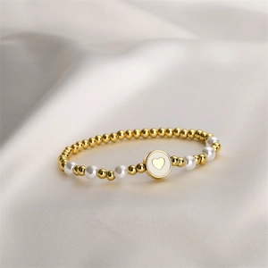 Gros plan d'un bracelet élastique avec perles dorées et pendentif cœur blanc sur soie