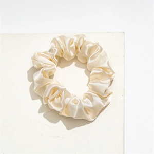 Detailed view of luxury champagne satin scrunchie on a white marble display stone