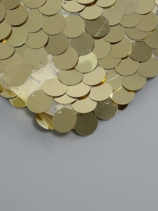 Macro detail of overlapping gold fish-scale sequins on fine mesh for party dresses