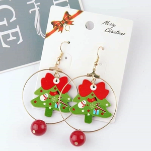 Detail of Christmas hoop earrings with green tree charms and red bow on a festive card