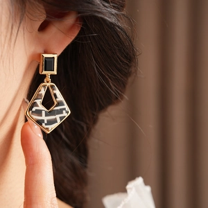 Close-up of luxury geometric rhombic earrings with black and checkered resin on a model