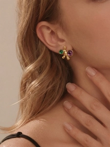 Détail de boucles d'oreilles branche dorée avec pierres vert émeraude et violet foncé