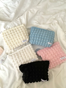Flat lay of bubble textured makeup bags in beige blue pink and black on white bedding