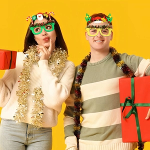 Two people wearing festive Christmas glasses with Santa and reindeer motifs on yellow background